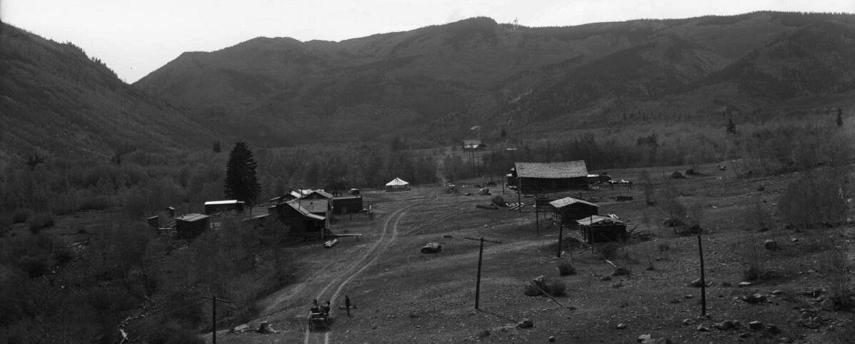 Panoramic photograph of Jasper, Colorado between 1910 and 1920, showing frame and log buildings along a dirt road in the valley with mountains behind