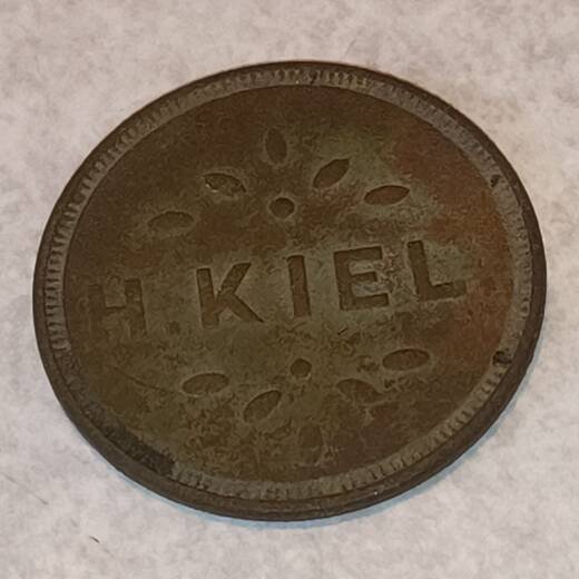 Worn brass token stamped H. KIEL between two sprays of leaves