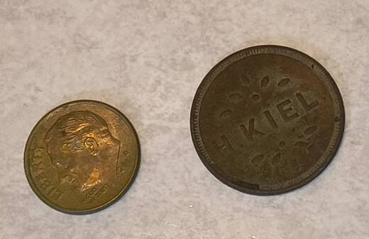 The H. Kiel brass token lying beside a modern United States dime on a white surface